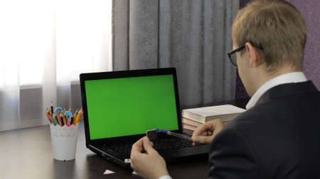 Male teacher looking at web camera making video call on laptop with green screen, chroma key. Working online from home. Distance education with children class on internet. Conference training webinarの写真素材