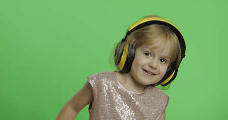 Girl in glossy dress and headphone listening to music and dancing. Happy four years old girl. Pretty little child, 3-4 year old blonde girl. Make faces and smile. Green screen. Chroma Keyの写真素材