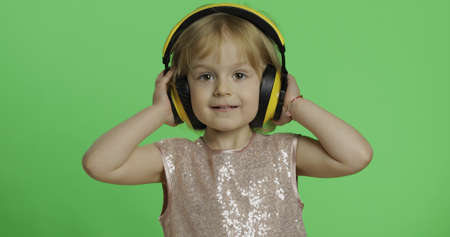 Girl in glossy dress and headphone listening to music. Happy four years old girl. Pretty little child, 3-4 year old blonde girl. Make faces and smile. Green screen. Chroma Keyの写真素材