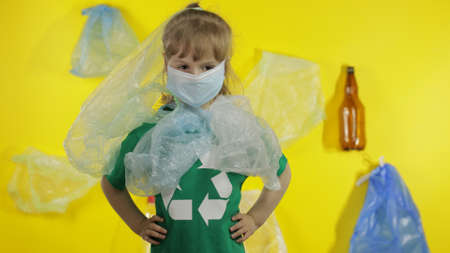 Junior girl activist in green t-shirt with recycle logo in plastic packages on her neck and head....