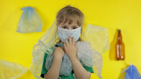 Sad girl activist in t-shirt with recycle logo in plastic packages on her neck and head. Background with cellophane bags, bottles. Reduce trash plastic pollution. Think green. Save ecology environmentの写真素材