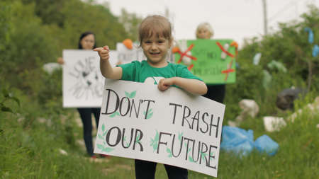 Girl volunteer holds encouraging protesting poster Dont Trash Our Future. Activists on background. Protests, chants. Forest park in cellophane bags, bottles. Plastic trash nature pollution. Recycleの写真素材