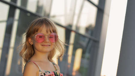 Kid girl at sunset wearing stylish sunglasses in airport. Tourist child in overalls with flowers. Hawaiian style look. Vacations, tourism, tripの写真素材