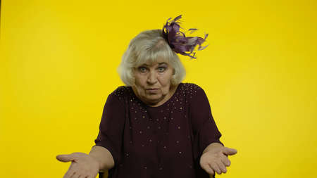 Confused irritated senior old woman raising hands, indignantly asking reason of failure, misunderstanding concept. Elderly stylish lady grandma asking what, why on yellow backgroundの写真素材