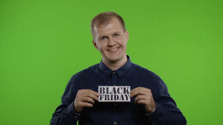 Happy shopper guy showing Black Friday inscription note, looking at camera amazed, rejoicing discounts in fashion store, purchase on big sale day. Studio shot on chroma key backgroundの写真素材