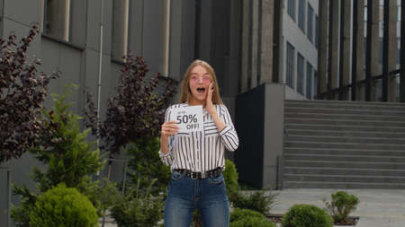 Excited girl in jeans showing Up To 50 percent Off inscription, advertising discounts, smiling...