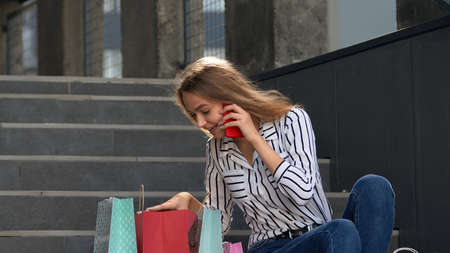Attractive young girl in shirt talking on smartphone about sales in shopping mall in Black Friday...
