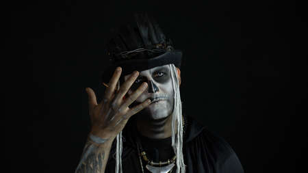 Man with horrible halloween skeleton makeup in costume with top-hat making faces, hiding behind his...