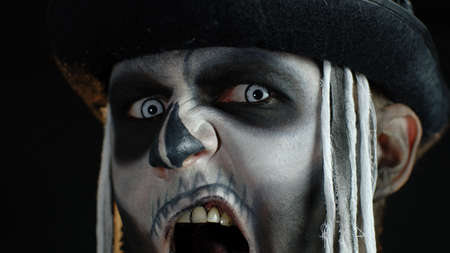 Close up footage of sinister man face with horrible Halloween skeleton makeup. Guy making faces,...
