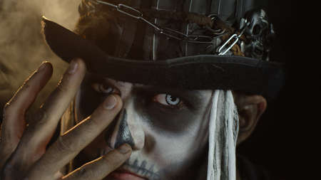 Close-up shot of man in skeleton Halloween cosplay costume. Guy in creepy skull makeup removing hand from face and looking wide open eyes. Day of The Dead. Isolated on black backgroundの写真素材