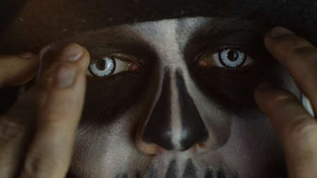 Close-up shot of man in skeleton Halloween cosplay costume. Guy in creepy skull makeup removing...