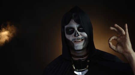 Scary man in skeleton Halloween cosplay costume. Guy executioner in creepy skull makeup looking at...