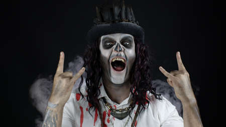Scary guy in thematic carnival costume of Halloween skeleton in bloody shirt, listening music,...