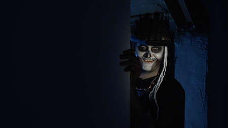 Creepy man with horrible Halloween skeleton makeup in costume with top-hat slowly appears from dark...