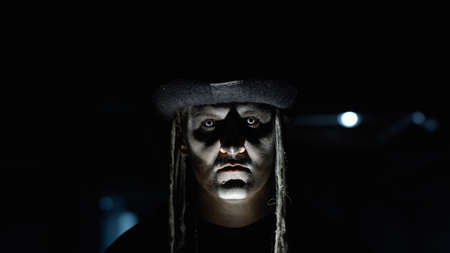 Frightening man face in carnival skull Halloween makeup of skeleton against dark parking hallway....