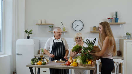 Elderly couple in modern kitchen interior. Grandmother and grandfather receiving organic vegetables from grandchild. Raw food eating diet. Senior healthy family lifestyle, World vegan day conceptの写真素材