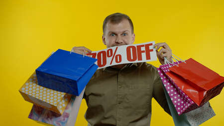 Joyful man showing Up To 70 percent Off inscription sign and shopping bags, smiling, looking...