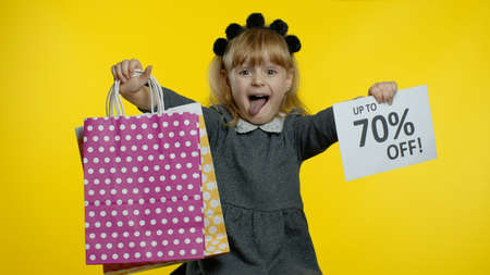 Joyful teen pupil girl with shopping bags showing Up To 70 percent Off banner text advertisement, showing tongue. Online shopping with low prices. Child kid rejoicing with holiday sale discountsの写真素材