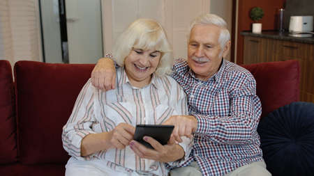 Happy smiling senior couple with tablet pc computer at home. Cheerful retired husband and wife...