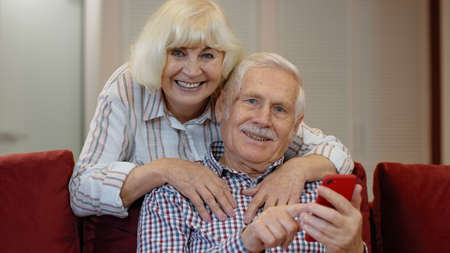 Senior old grandparents couple talking and using digital mobile phone at home. Online shopping....