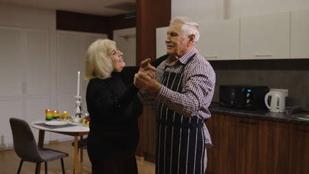 Happy senior couple in love dancing. Romantic evening supper with wine and candles, celebrating...