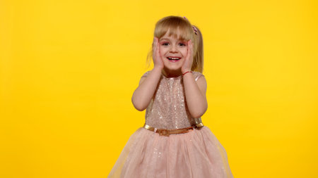Wow reaction. Portrait of happy amazed astonished young kid girl in shiny dress isolated on yellow copy space background. Impressed child. Perfect surprise. Exciting newsの写真素材
