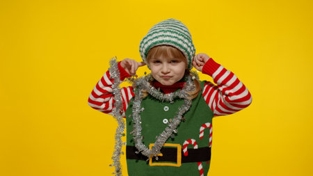 Displeased little blonde kid teen teenager girl in Christmas elf Santa helper costume isolated on yellow studio background. Child looking unhappily angry, sad at camera. Negative emotions and reactionの写真素材