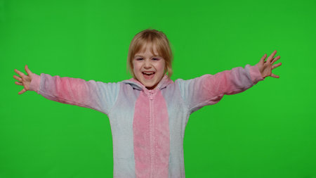 Young little blonde child 5-6 years old smiling, dancing, celebrating, making faces in unicorn costume on chroma key green background. Portrait of kid girl animator in unicorn pajamas. Slow motionの写真素材