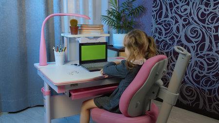 Child girl studying homework during online lessons at home. Kid making video call. Laptop green screen. E-learning, webinar.の写真素材