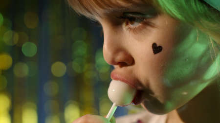 Close-up shot of stylish teenager caucasian kid girl lips licking lollipop with tongue. Child in...