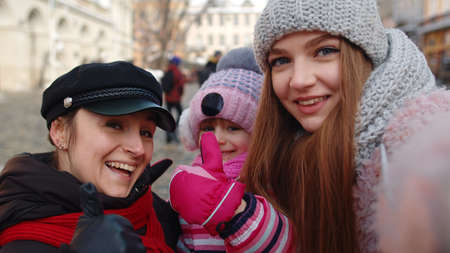 POV shot of sisters couple taking selfie, posing, making video conferencing on mobile phone together with younger sister child girl. Woman tourists talking, embracing. Family winter holiday vacationsの写真素材