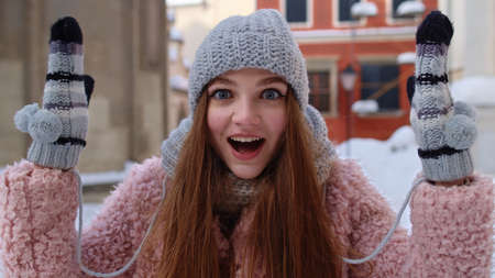 Excited young woman looking to camera, opening her mouth in amazement, shouting wow on winter city street. Caucasian pretty girl raising hands in surprise shocked by sudden victory. Positive emotionsの写真素材