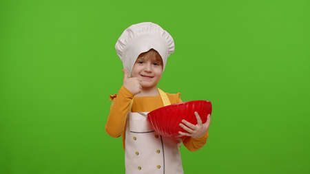 Portrait of little child girl kid dressed as professional cook baker chef mix dough in bowl, prepare cake on chroma key background. Nutrition, cooking school, education, food. Fun, humorの写真素材