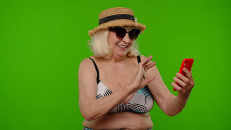 Mature woman traveler blogger in sunglasses, taking selfie portrait photo, video call on smartphoneの写真素材