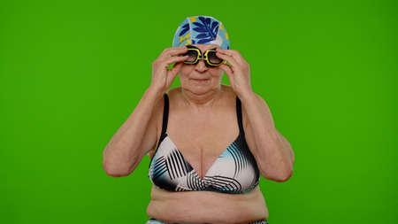 Senior woman tourist wearing swimming glasses, looking at camera, dancing on chroma key backgroundの写真素材