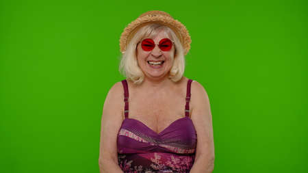 Senior woman traveler on vacation in red sunglasses, looking at camera, smiling, starting laughing