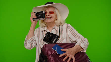 Senior woman tourist photographer taking photos on retro camera and smiling on chroma key backgroundの写真素材