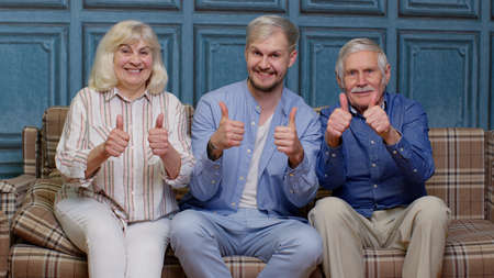 Family of senior grandparents with adult son showing thumbs up gesture having fun looking at camera