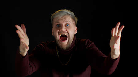 Stylish young man with blue eyes shout loudly, wins competition achieves goal, makes triumph gesture, guy says yes feels like winner shows fist, happy dream come true on black studio backgroundの写真素材