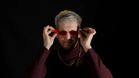 Portrait of seductive young man in trendy stylish clothes wearing sunglasses on black background. Fashion people sincere emotions lifestyle. Attractive guy studio shot. Fun, enjoyment, slow motionの写真素材