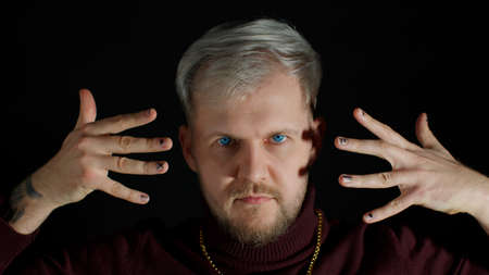 Stylish young man with blue eyes in trendy clothes looking at camera through the fingers, posing,...