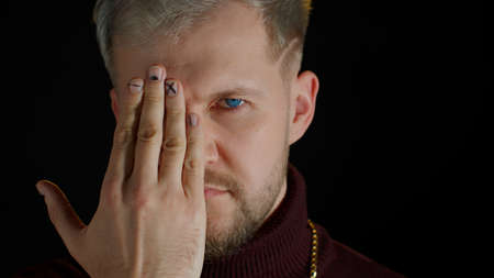 Confident stylish man in sensually looking at camera through the hand with one eye, posing, feeling...