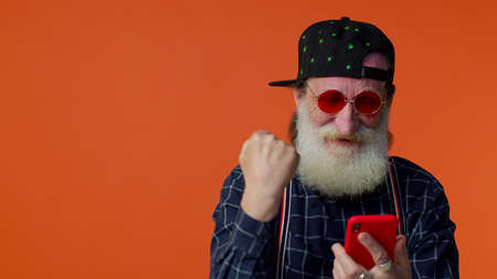 Happy excited joyful elderly bearded gray-haired man use mobile cell phone typing browsing say wow...