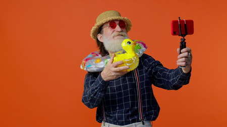 Mature grandfather traveler blogger with swimming ring and inflatable duck toy, taking selfie on...