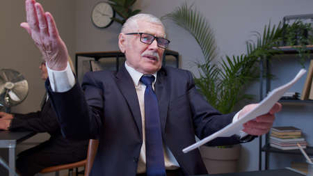 Irritated elderly man boss raising hands in questioning gesture why what in office room. Mature...