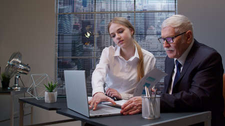 Woman secretary talking on mobile cell phone with client. Busy senior business man boss entrepreneur working, analysis financial graph data in office. Girl having conversation on telephone. Team workの写真素材