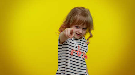 You and me here and right now. We are team. Little child girl looking authoritative, fingers down, demanding immediate serious conversation, giving command. Kid children on yellow studio backgroundの写真素材