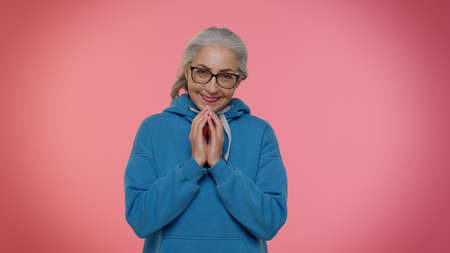 Cunning sneaky mature granny woman with tricky face gesticulating and scheming evil plan, thinking over devious villain idea, cunning cheats, jokes and pranks. Senior grandmother on pink backgroundの写真素材