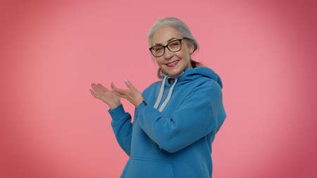 Come here to us. Elderly good-looking granny woman showing inviting gesture with hands, ask to join,...