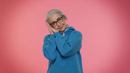 Elderly granny gray-haired woman yawning, sleepy inattentive feeling somnolent lazy bored gaping suffering from lack of sleep. Senior old grandmother isolated on pink background. People emotionsの写真素材